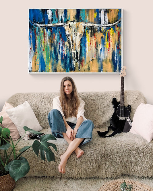 A girl sitting in her rooms sofa with a guitar and a large abstract hand painted original wall art 