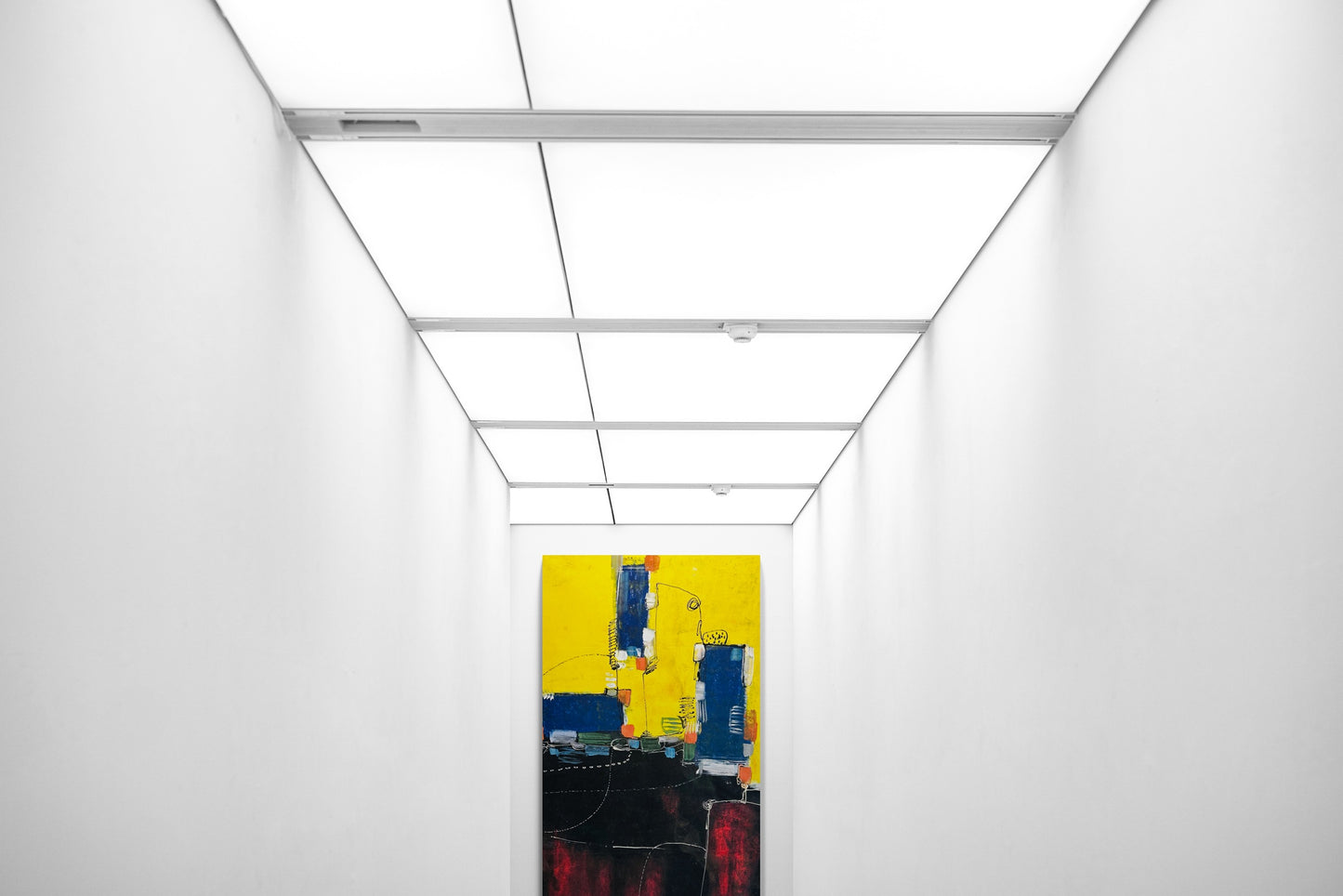 Large abstract hand painted wall art in a hallway with fluorescent ceiling light panels