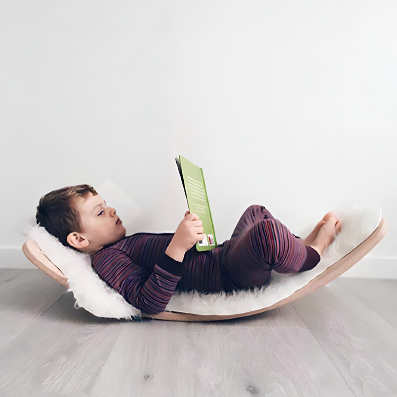 A toddler enjoys the Wooden Balance Board Montessori Toy, using it as a rocking bed while immersed in a book.