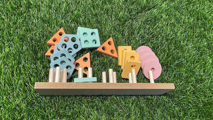 A Montessori educational wooden stacking toy with colorful rings in different shapes, laying on the lawn on a sunny day.